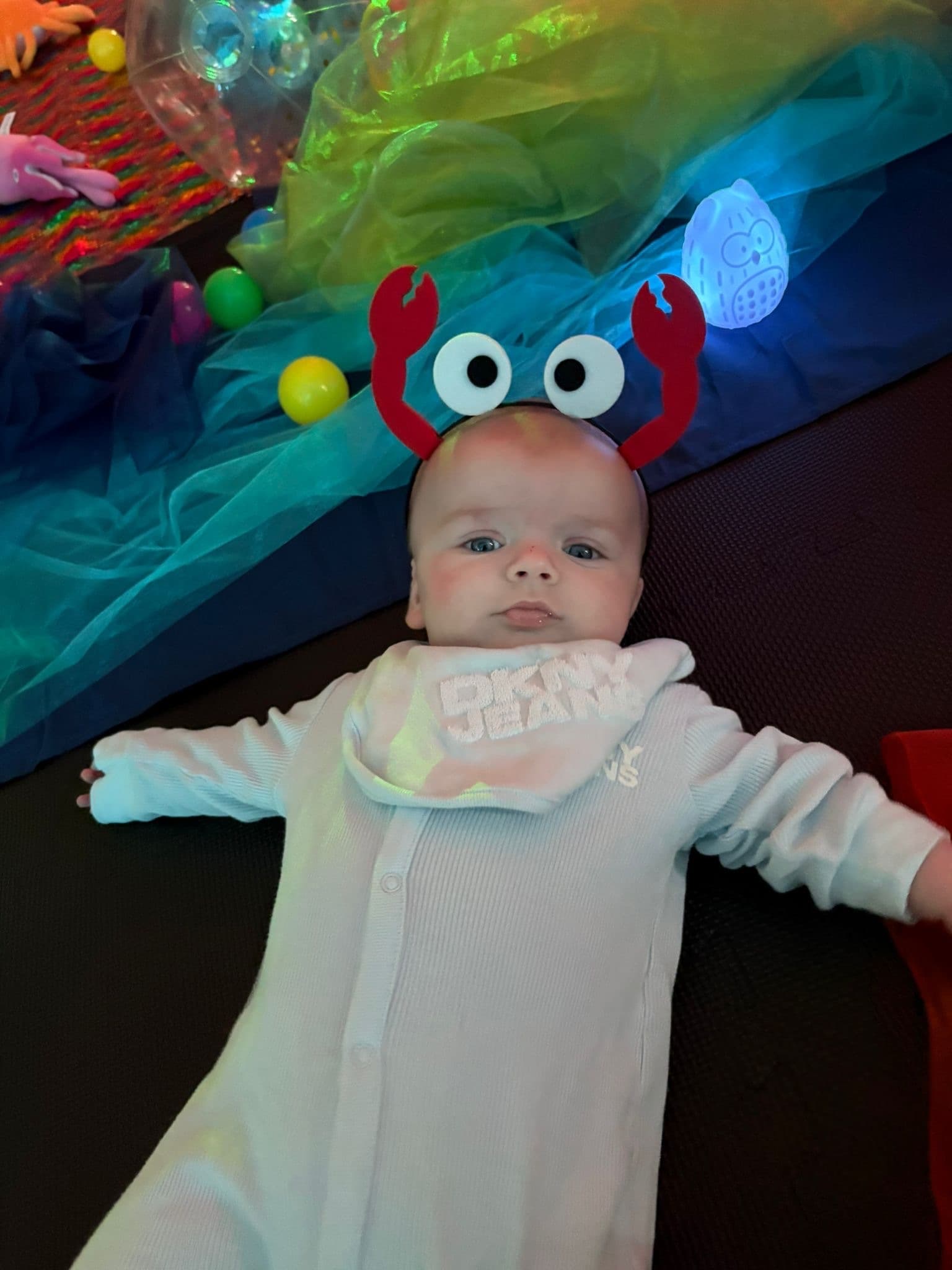 Baby in sensory play with crab headband and glowing toys