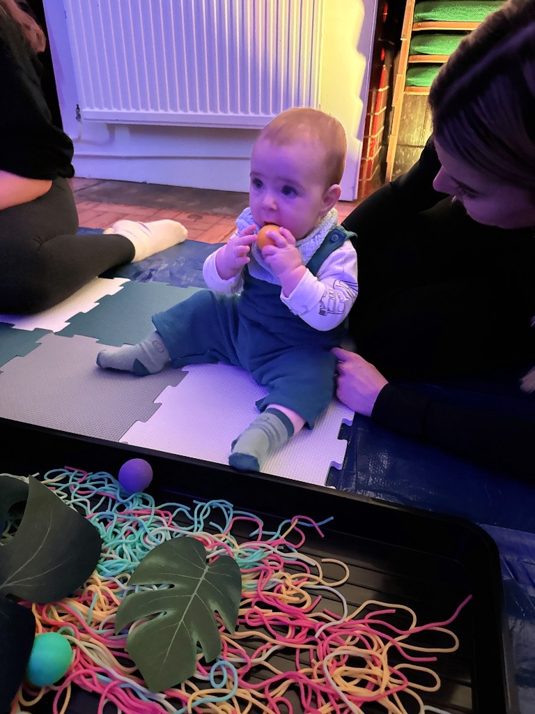 Toddler exploring messy play with noodles and leaves